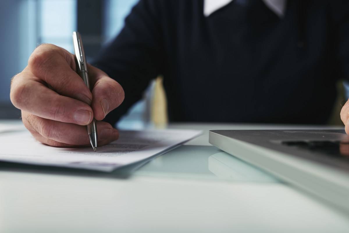 Main qui relit et signe un contrat de sous-traitance posé sur un bureau