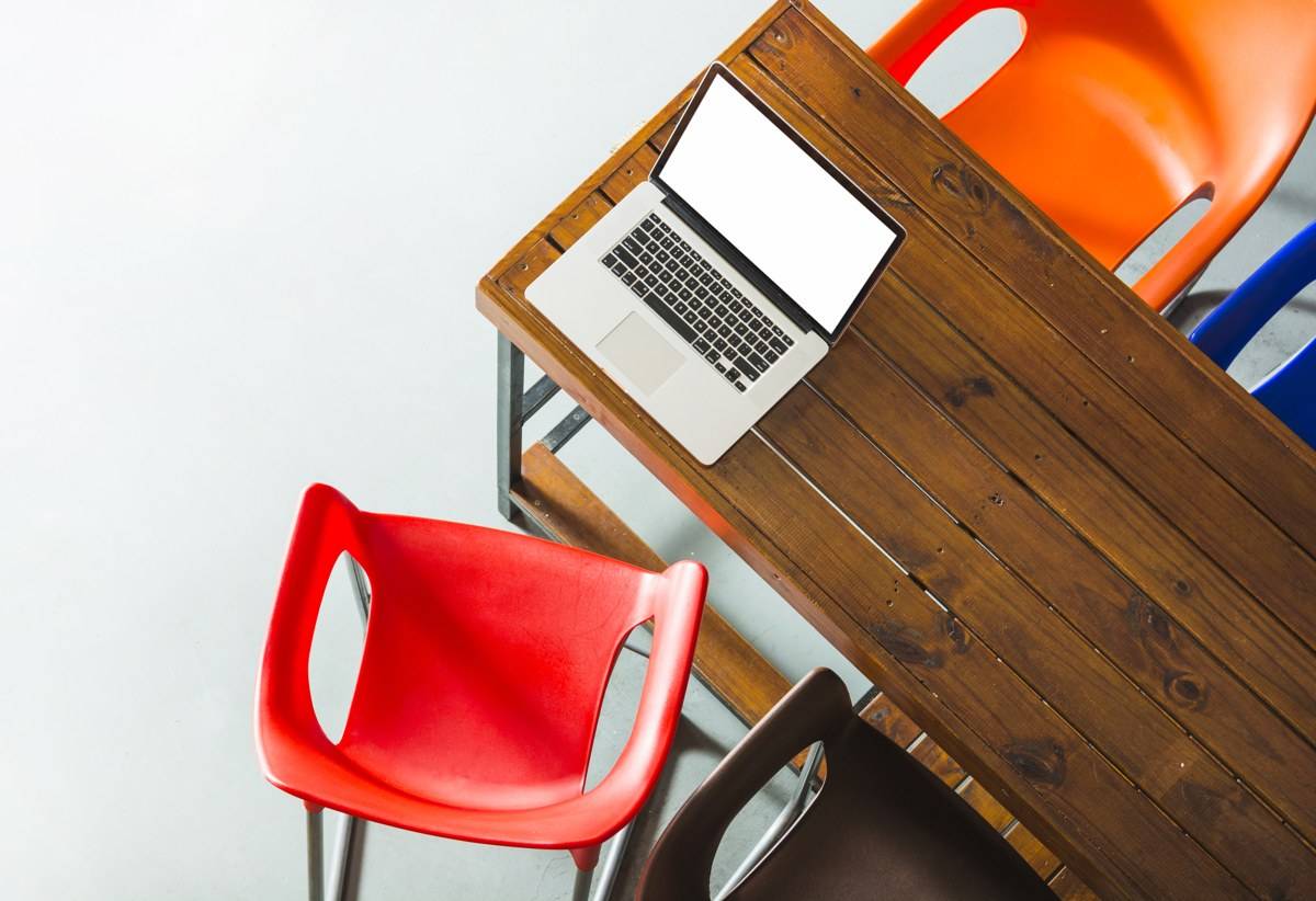 Ordinateur portable ouvert sur une table en bois entourée de chaises colorées